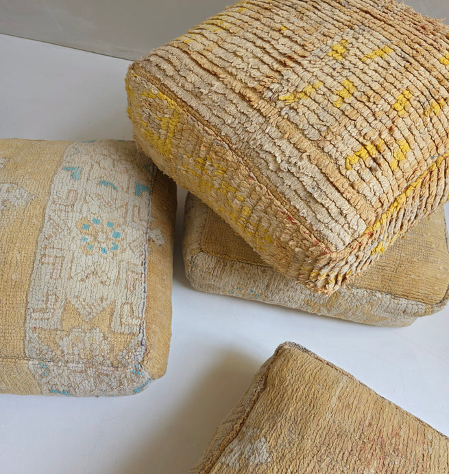 A collection of vintage wool floor cushions with yellow patterns, made from repurposed rugs.